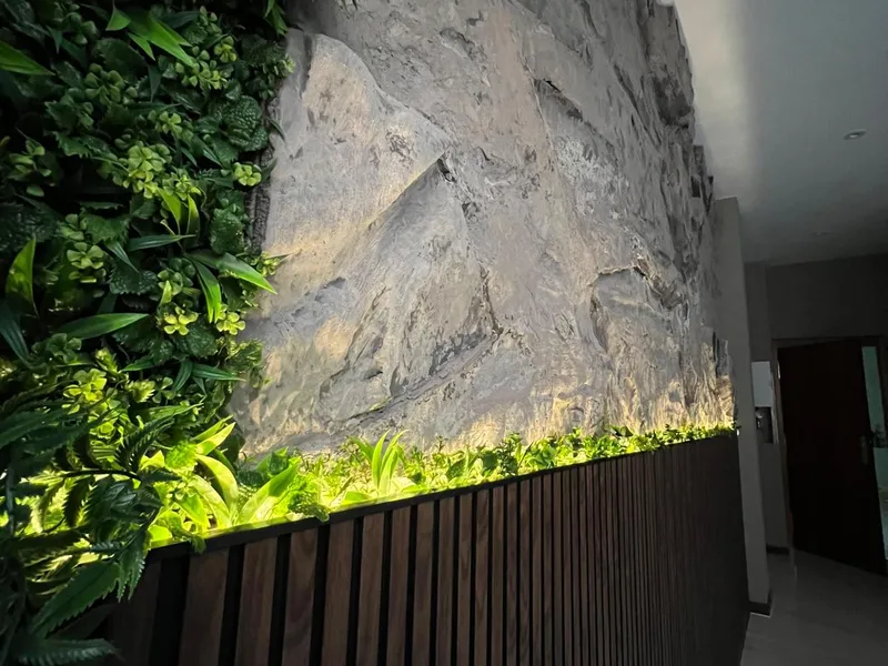 Pared de piedra natural iluminada con jardín vertical y listones de madera