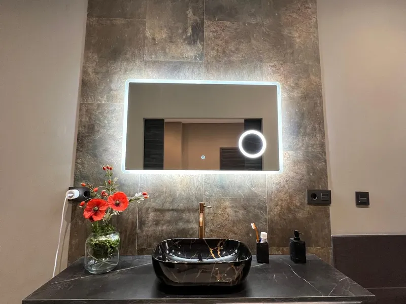 Lavabo sobre encimera negra con espejo retroiluminado y frente de microcemento