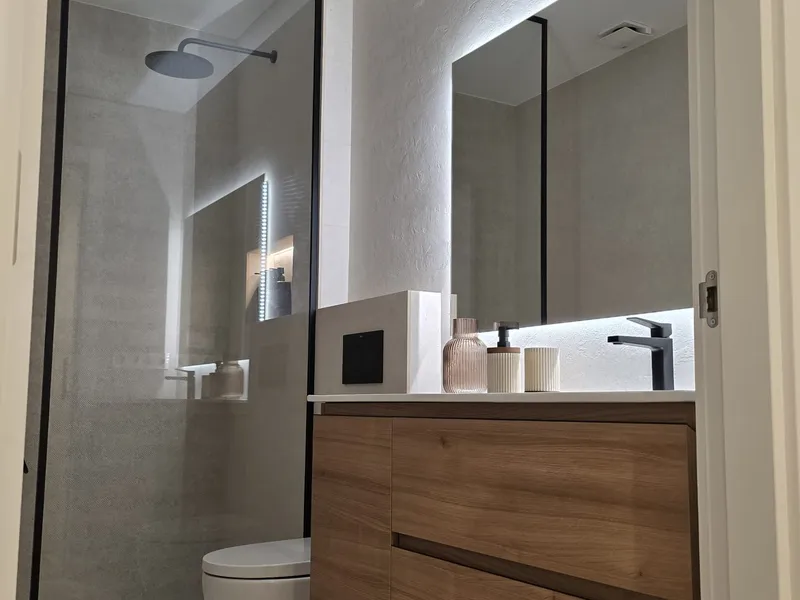 Baño terminado con ducha de obra, mampara negra y mueble de madera